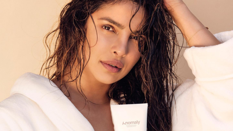 Priyanka Chopra Jonas in a white robe with wet hair holding an Anomaly tube for her India haircare brand growth.