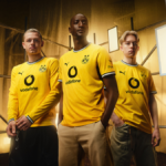 Three men wearing the yellow 2026/27 Borussia Dortmund home kit on an industrial scaffold set for the global launch
