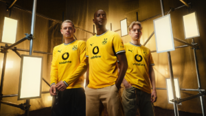 Three men wearing the yellow 2026/27 Borussia Dortmund home kit on an industrial scaffold set for the global launch