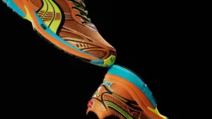 PUMA Homura runner in orange and yellow with PUMALITE cushioning and turquoise accents on a black background.