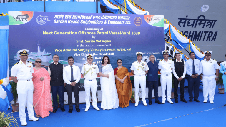 The new warships built to secure India trading routes 4 Indian Navy officers, Smt. Sarita Vatsayan and dignitaries standing in front of a blue Sanghmitra Yard 3039 launch banner.