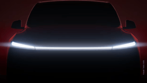 Dark silhouette of a Tesla SUV facing forward with a single, continuous white LED light bar illuminated across its front end.