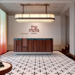 Wooden reception desk under a long pendant light with patterned tiles in a colonial-style hotel lobby in Singapore.