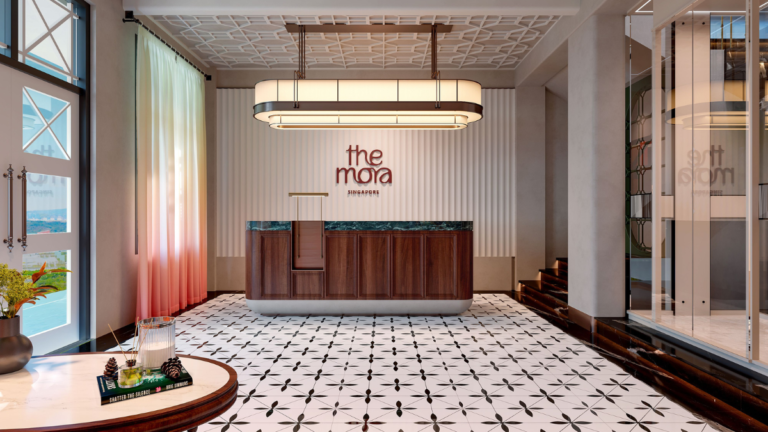 Wooden reception desk under a long pendant light with patterned tiles in a colonial-style hotel lobby in Singapore.