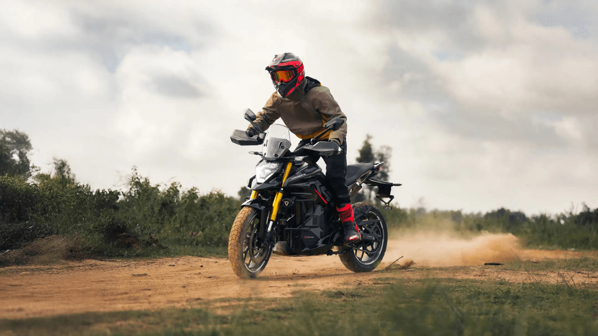 Rider in a tan jacket and red helmet on a black Ultraviolette electric motorcycle kicking up dust on a dirt track in India.