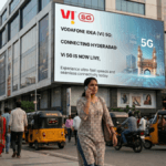 A woman uses a phone on a Hyderabad street with auto-rickshaws below a giant digital Vi 5G billboard.