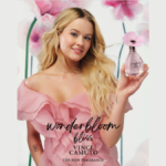 Woman in pink ruffled dress holds Vince Camuto Wonderbloom Bliss bottle with soft petal cap. Pink paper flowers are in bac...