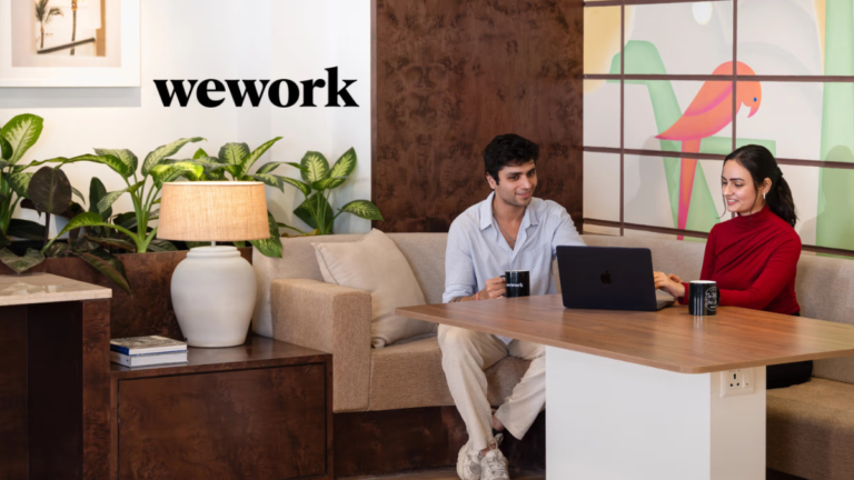 Two people using a laptop in a modern lounge with a bird mural at the WeWork Worldmark 6 office in Aerocity.