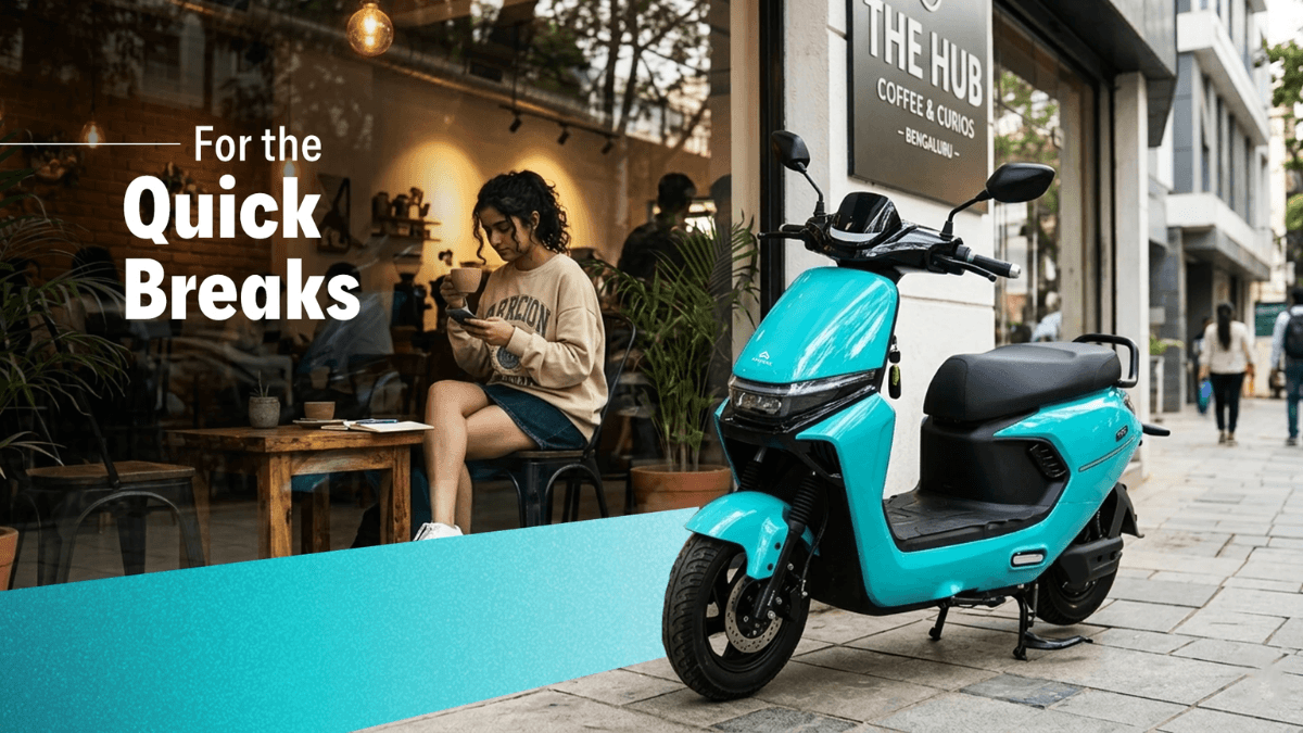 At ₹69,499 this scooter skips RTO queues entirely 1 A cyan Ampere Reo VYB scooter parked outside a Bengaluru cafe with a woman sitting indoors looking at her phone.