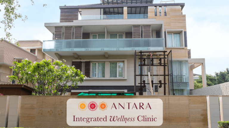 Exterior of a modern building with glass balconies and an Antara Integrated Wellness Clinic signboard in Gurugram.