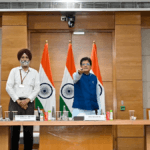 Piyush Goyal pressing a remote at a desk alongside three officials and Indian flags, inaugurating the BHAVYA portal.