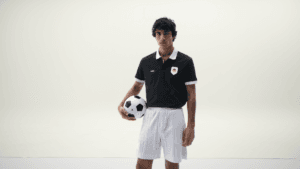 Man holding a football wearing a black BOSS polo with a Germany flag badge and white shorts from the fanwear lineup.