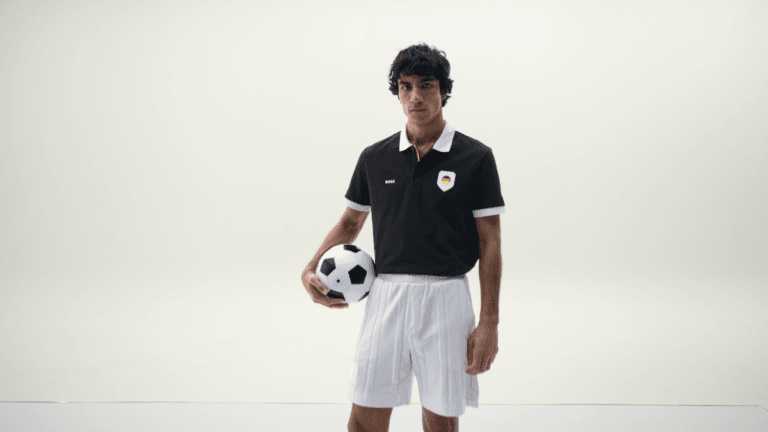 Man holding a football wearing a black BOSS polo with a Germany flag badge and white shorts from the fanwear lineup.