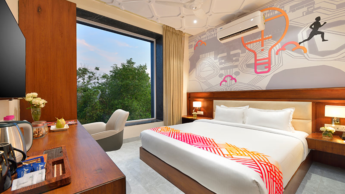 At ₹3,399 a night, IHCL brings lean luxury to Gadchiroli 1 Wooden desk with tea kettle beside a king bed with a colourful runner facing a large window showing green trees.