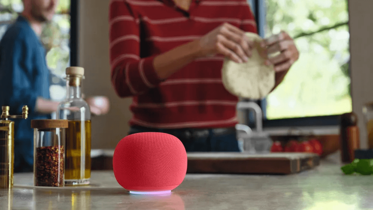 The smart speaker that remembers what you just said 2 Red Google Home Speaker on a kitchen counter while a person prepares dough in the background, showing home utility.