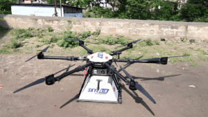 A multi-rotor drone with a Skye Air delivery box attached underneath resting on dirt, deployed for India Post.
