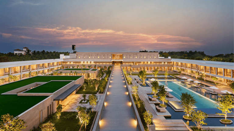 Symmetrical aerial view of a luxury resort courtyard featuring a large swimming pool, lighted central walkway, and lawns a...