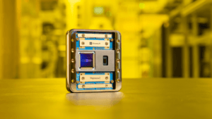 The gold-cased Microsoft Majorana 2 quantum chip sitting on a surface in a yellow-lit lab, marking a leap in AI research.