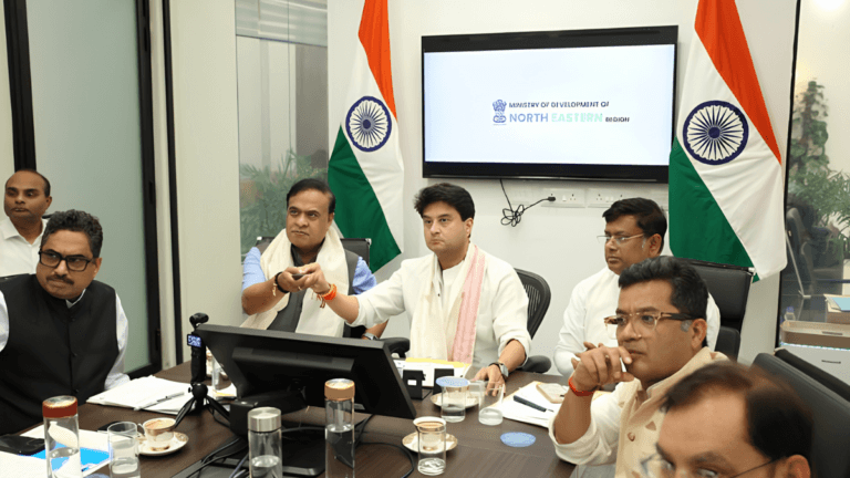 Indian officials pressing a button at a conference table with national flags, launching the Muga silk Mission Senehjori.