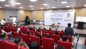 Ashwini Vaishnaw speaking at a podium to an auditorium of students at MNIT Jaipur for a tech event.