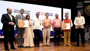 Dignitaries standing on a stage holding signed document folders at the Navachar Mantra event at IIT Delhi.