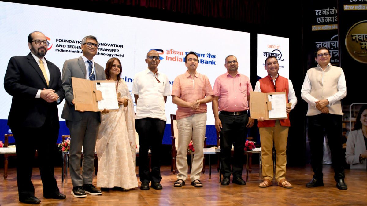 Dignitaries standing on a stage holding signed document folders at the Navachar Mantra event at IIT Delhi.