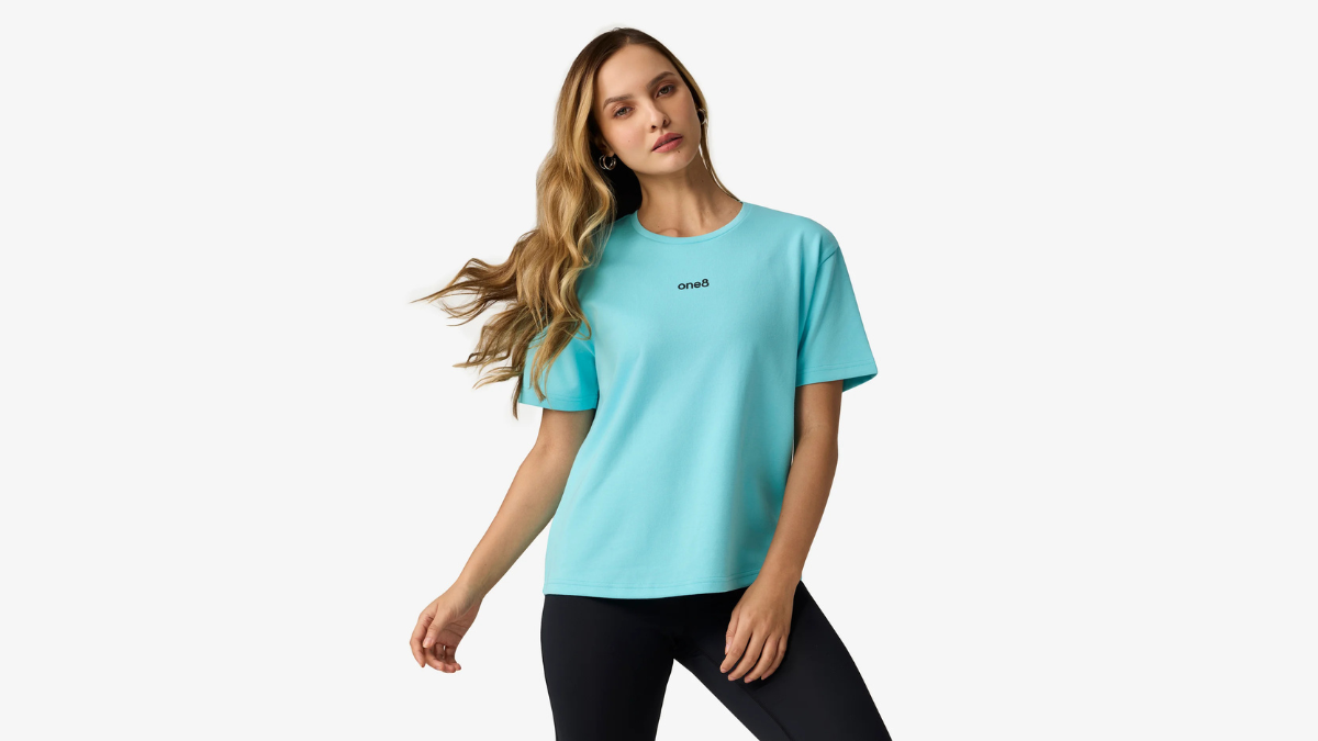 The cricket captain leaves a ₹300 crore deal to go solo 1 A woman posing in a light blue t-shirt with a small chest logo and black leggings against a white background, activewear.