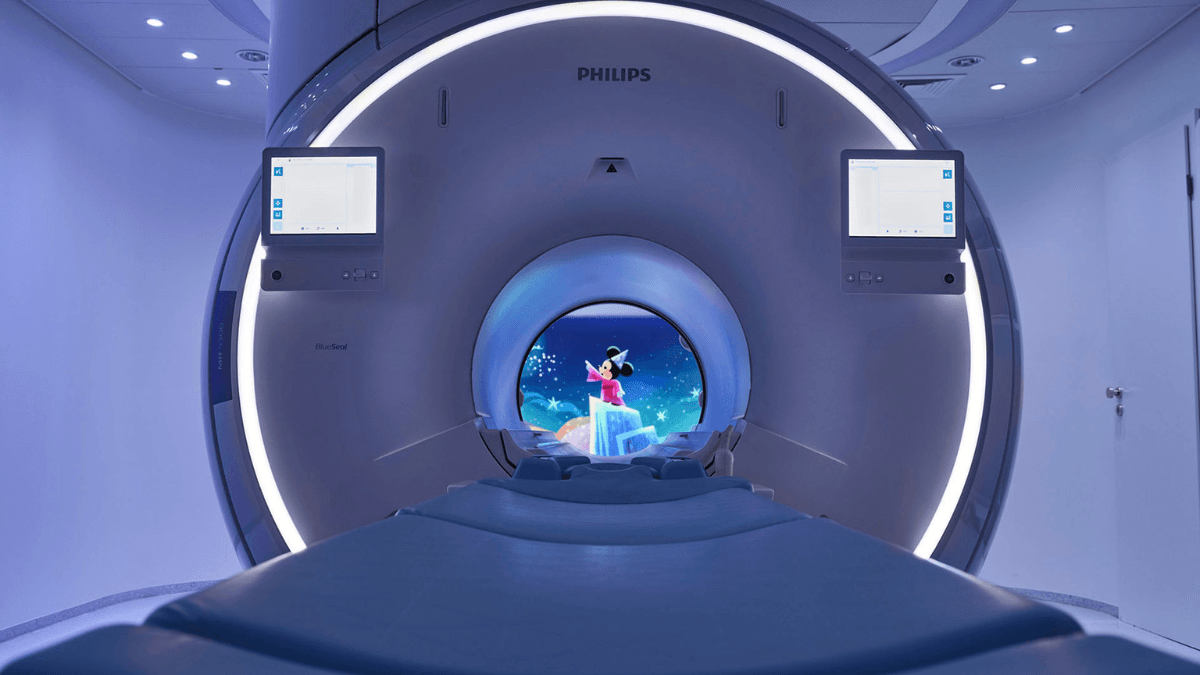 A front view of a Philips MRI scanner with a Mickey Mouse cartoon projected inside the circular bore of a blue lit room.