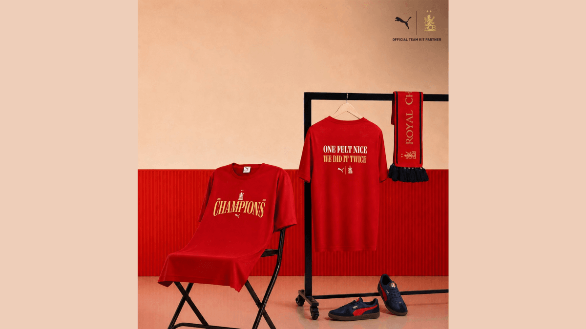 The championship merchandise to grab before it sells out 1 Red PUMA x RCB Champions tee on a chair and clothing rack showing tournament victory text for the Indian market drop.