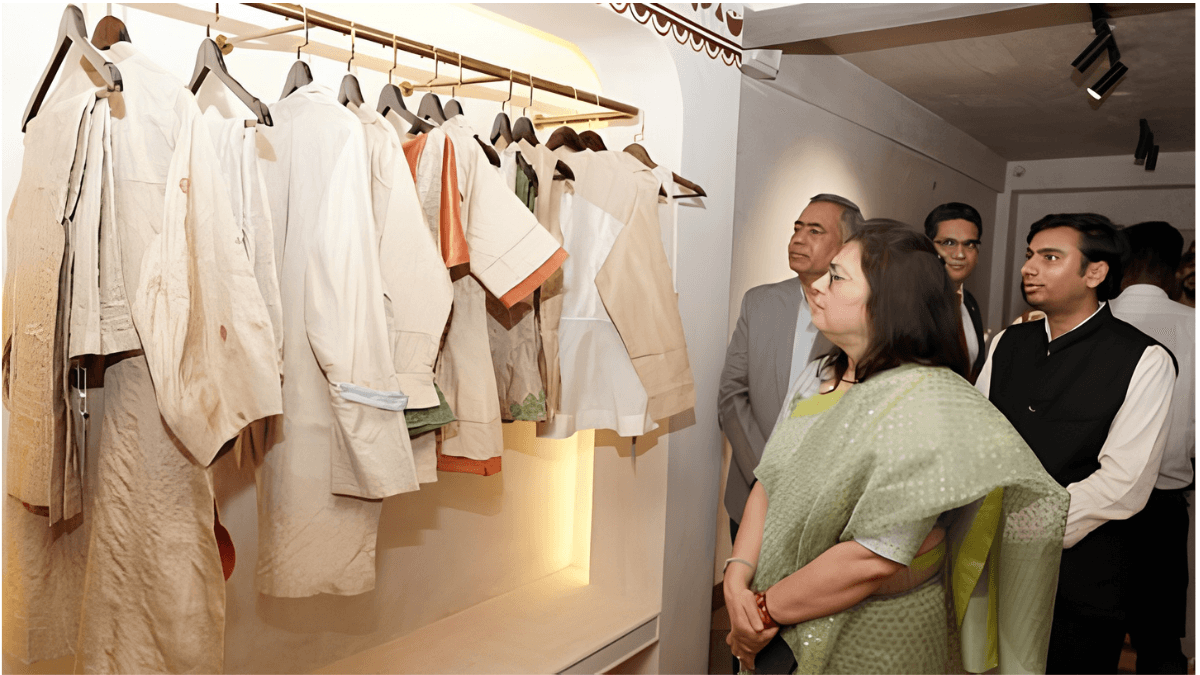 TRIFED opens a premium tribal textile store in New Delhi 2 A woman in a green saree and men look at off-white handloom garments on a clothing rack at the TRIFED retail opening.