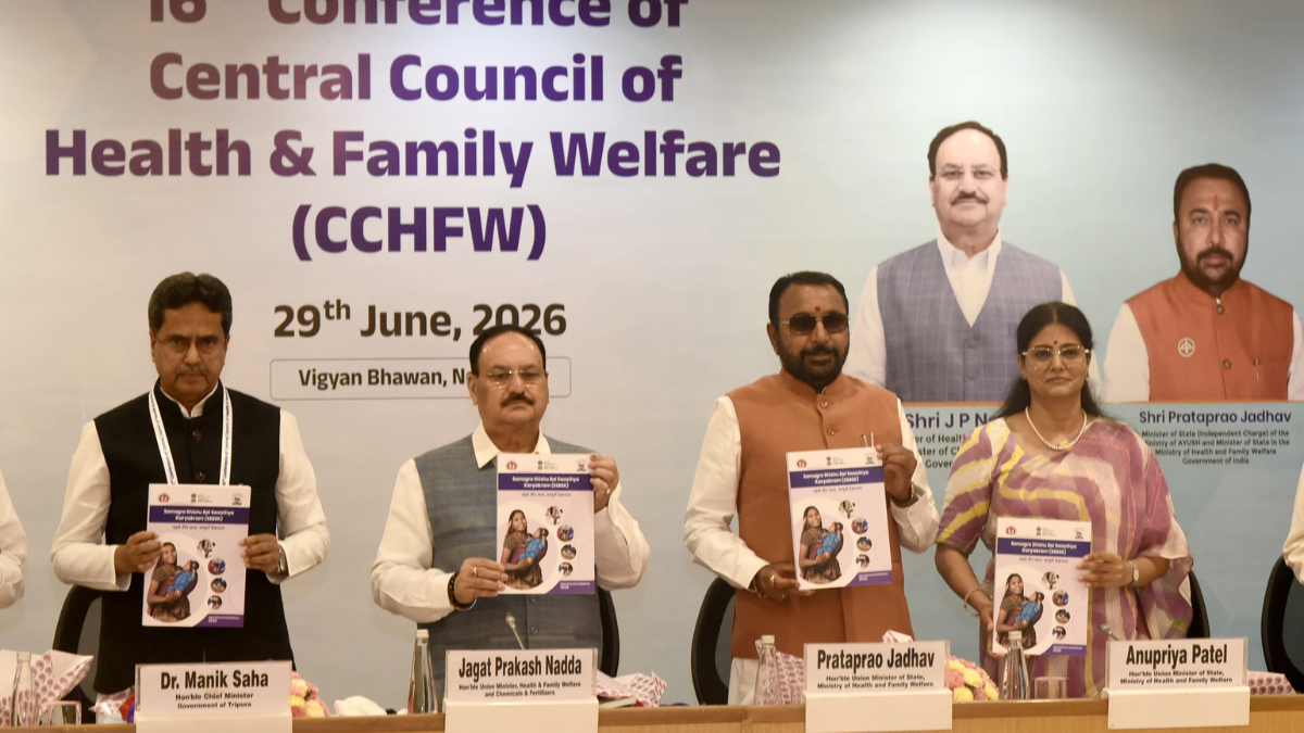 Four Indian health officials stand behind a table holding copies of the SSBSK child health care booklet.