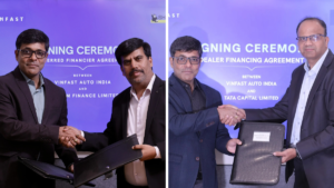 Men in suits shake hands and hold black folders in front of purple signing ceremony backdrops for VinFast India.