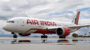 Air India Boeing 787 widebody aircraft parked on a wet runway reflecting the white and red fuselage under a cloudy sky.