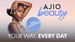 Woman with blue eyeliner and nail art posing beside an AJIO Beauty promotional banner with Just Launched badge.