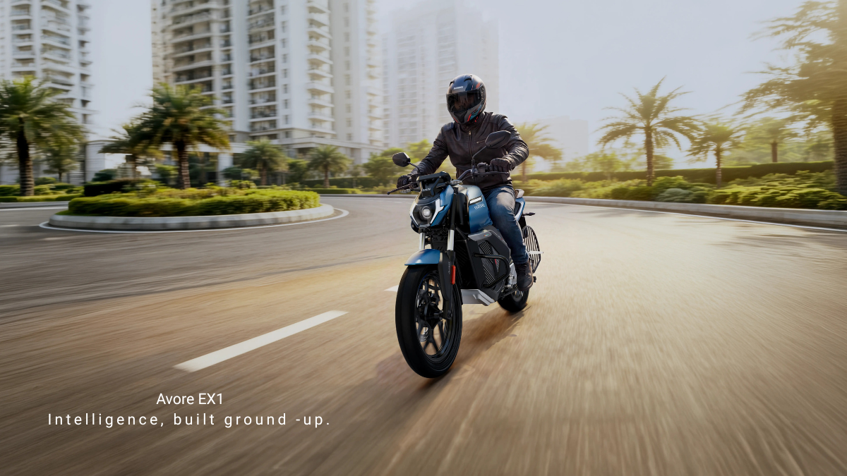 Can a standard wall socket power a 260km electric bike 2 Rider navigating a blue Avore EX1 electric motorcycle around a curved road near residential apartment blocks.