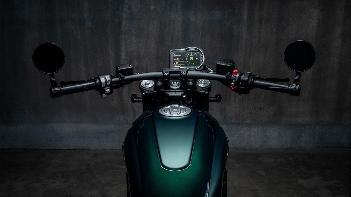 Top-down view of a motorcycle handlebar with round bar-end mirrors, a digital display screen, and a green fuel tank.