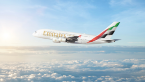 Emirates Airbus A380 aircraft flying left to right over a white blanket of clouds under a blue sky, representing aviation.