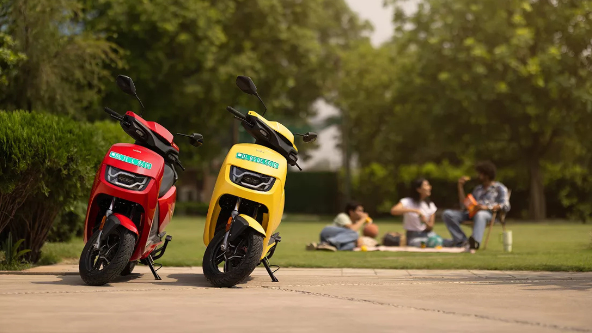 This record-breaking scooter cuts daily running costs 2 Red and yellow VIDA electric scooters parked on a stone pavement with people sitting on a lawn in the blurred background.
