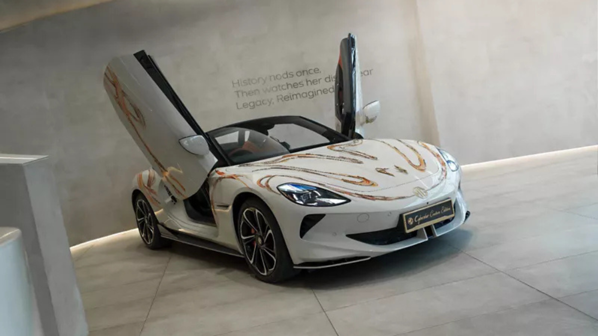 Couture Edition M9 and Cyberster EVs arrive at INR 84.94 Lakh 1 White convertible sports car with open scissor doors and bonnet graphics parked on tiled floor indoors.