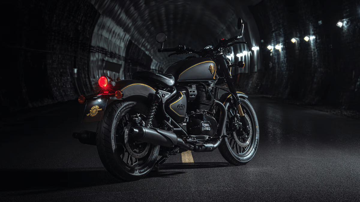 Rear three-quarter view of a black motorcycle with a lit red taillight parked inside a dark concrete tunnel.