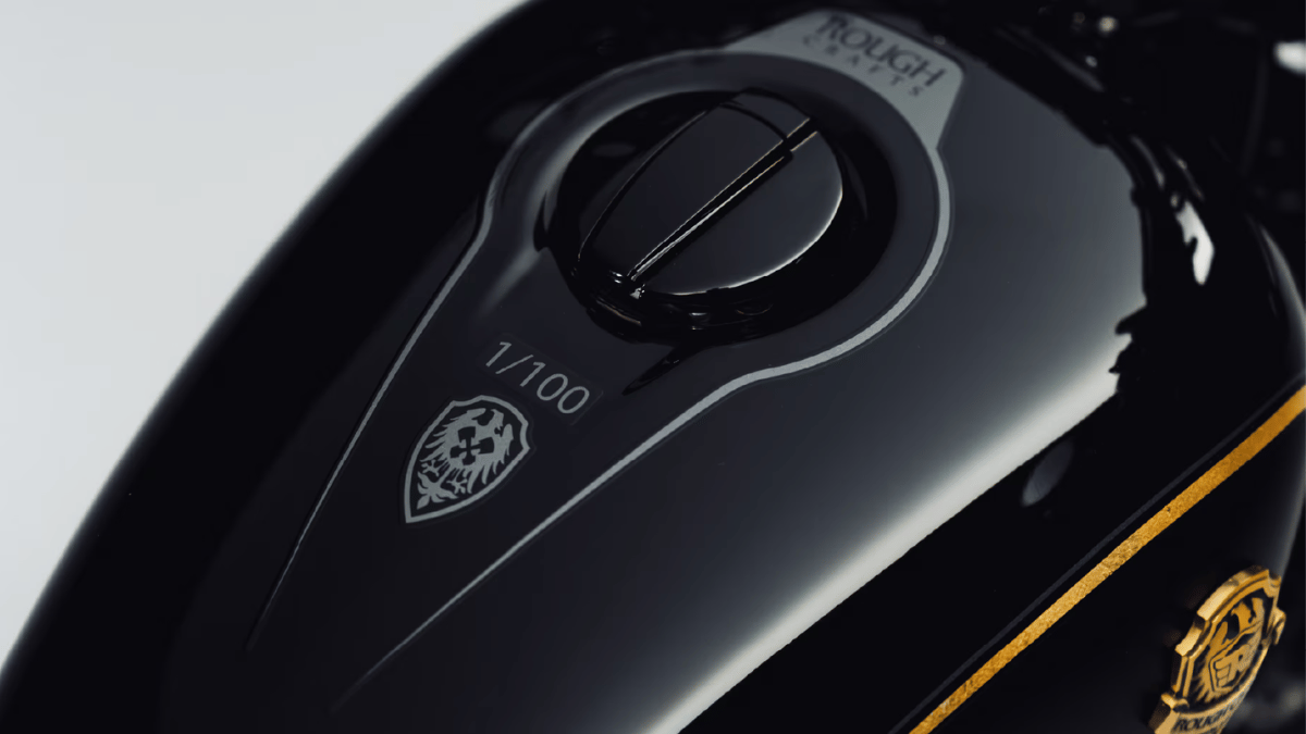 Close-up of a glossy black motorcycle tank showing a grey shield badge and painted text reading one of one hundred.