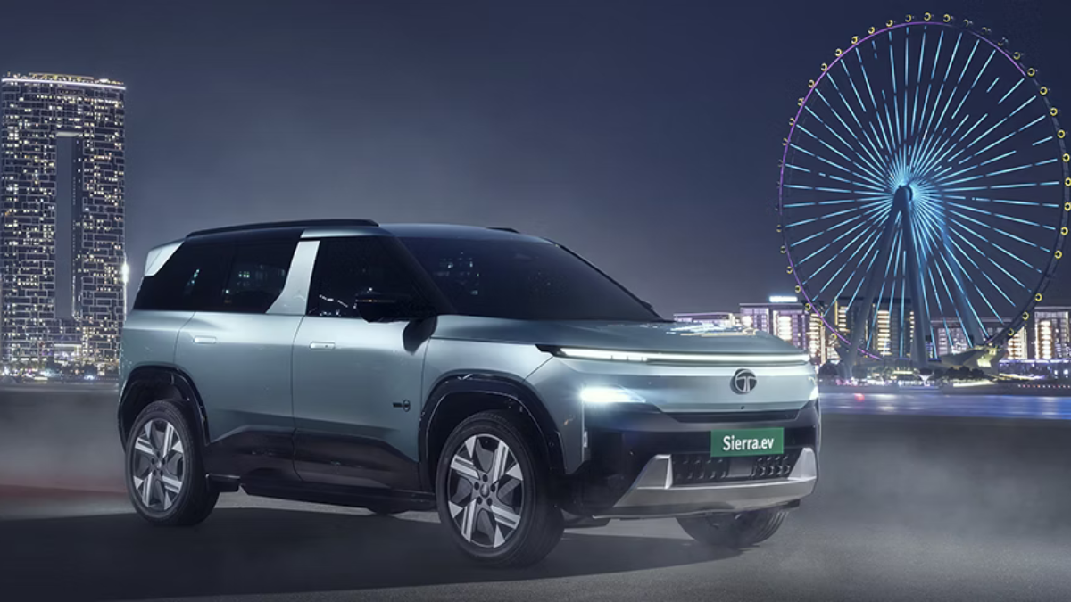 A classic nineties design brings theatre tech to your drive 2 Silver electric SUV parked at night with a lit skyscraper on the left and an illuminated Ferris wheel on the right.
