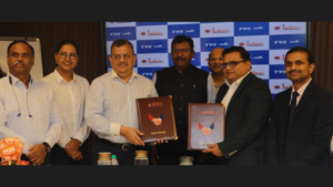 Seven corporate executives standing in front of a blue TVS and Indane logo banner, holding signed agreement folders.