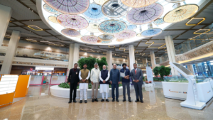 Dignitaries including Narendra Modi stand in a brightly lit terminal lobby below colourful circular ceiling patterns airport.