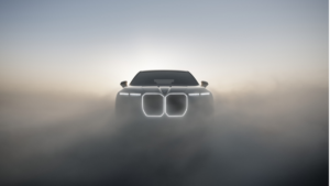 Dense mist surrounding lit split headlights and glowing kidney grille on dark BMW 7 Series front silhouette sedan.