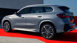 Alloy wheels on red floor, silver BMW X1 Long Wheelbase side profile, grey concrete wall under clear sky luxury SUV.