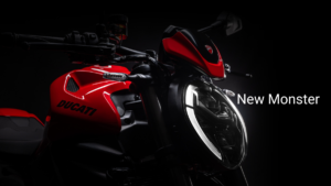 Red Ducati Monster V2 fuel tank and curved LED daytime running headlight on dark backdrop.