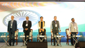 Five officials standing on stage behind glass tables before an Indian tricolour screen at the E-Samudra launch event.