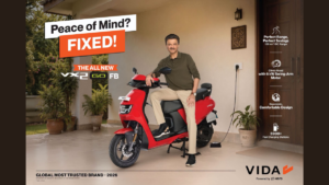 Red electric scooter connected to a wall socket beside a seated man in an olive shirt on a house porch mobility.