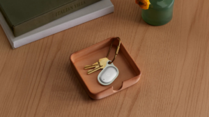 Grey Google Pixel Tag attached to brass key ring sitting inside terracotta square valet tray next to book hardware.